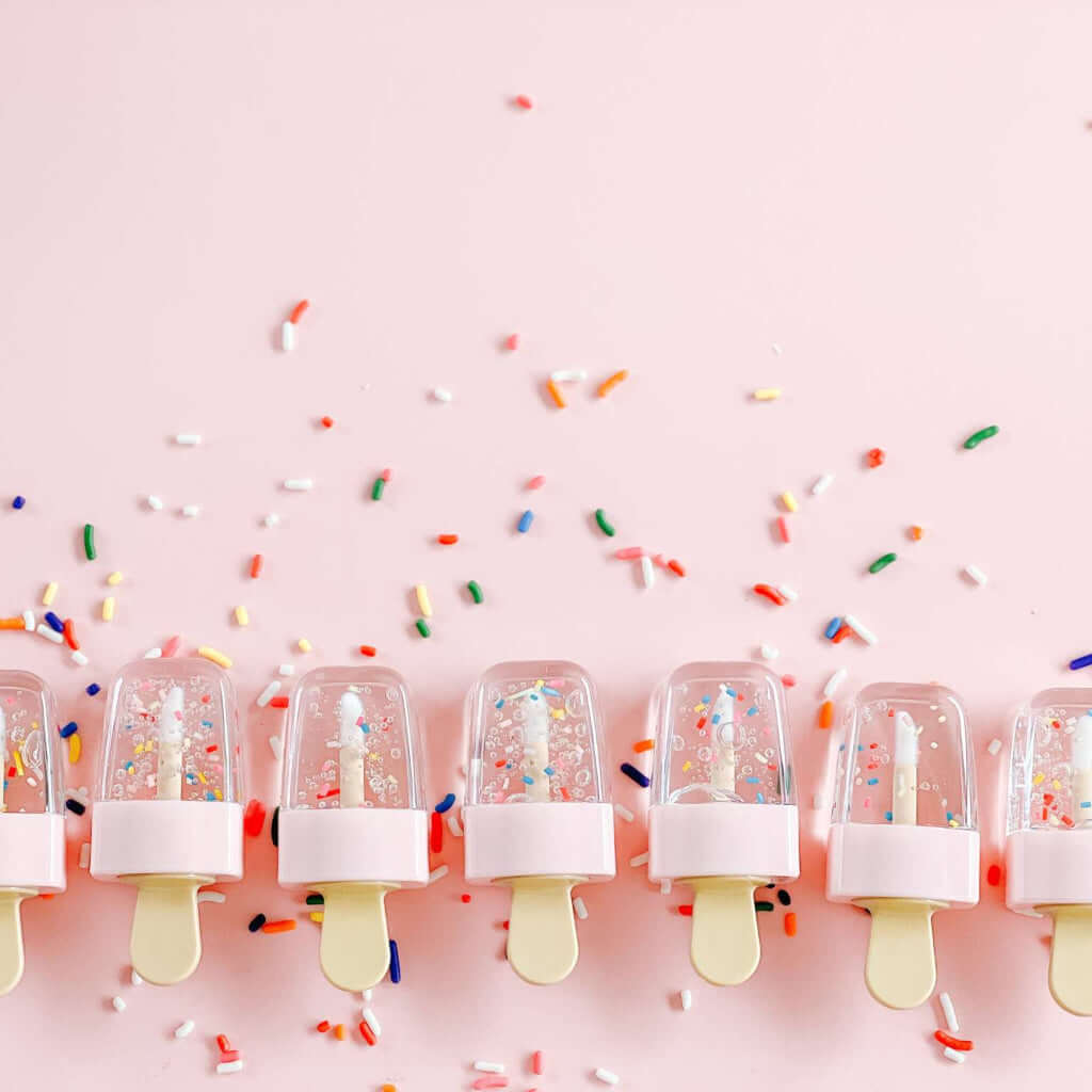 Chocolate scented lip gloss with colorful sprinkles on a pink background.