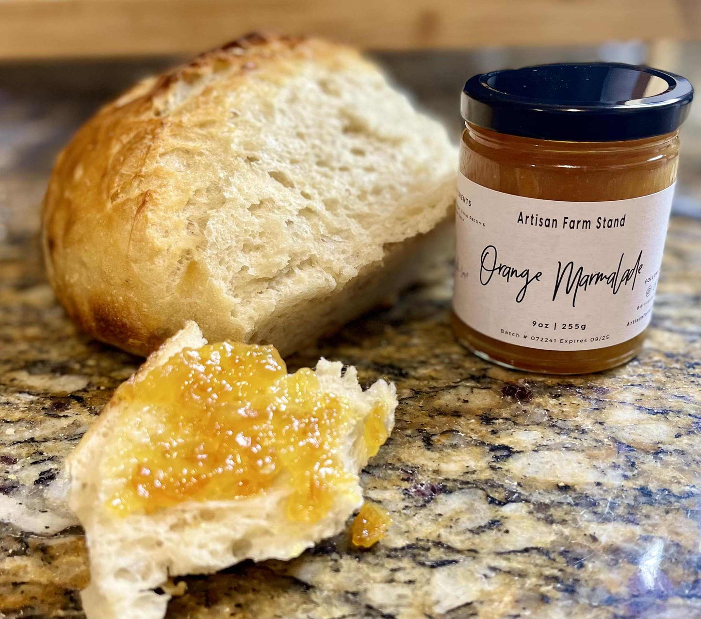 Orange marmalade jar next to freshly baked bread with spread on stone surface.