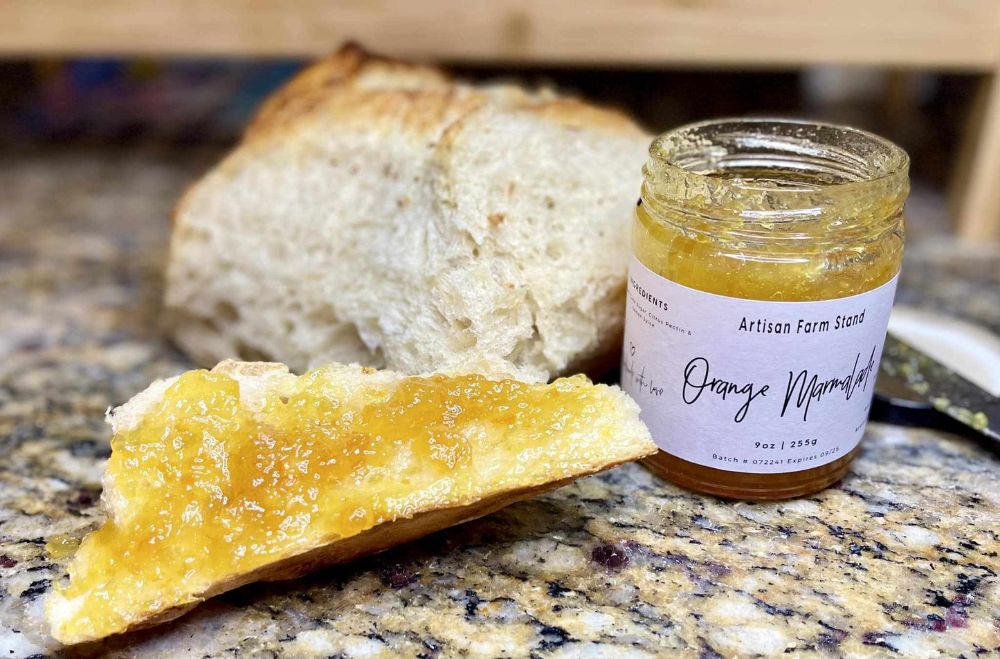 Artisan Farmstand Orange Marmalade jar next to a slice of bread with marmalade spread.