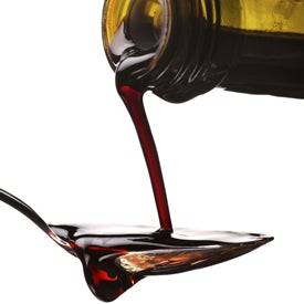 Balsamic Vinegar being poured from a bottle into a glass with a white background