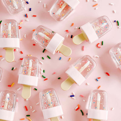Chocolate scented sprinkle pop lip gloss with playful sprinkles on a pink background.